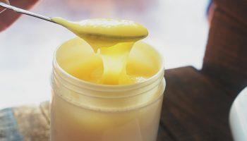 A closeup image of a spoon dipping into a jar of royal jelly product