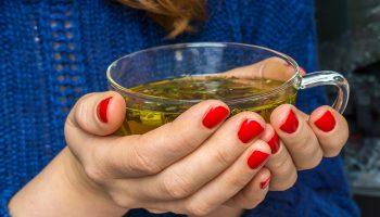 Woman in a blue-coloured sweater holding a transparent cup that contains green tea