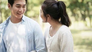 A man and a woman walking in a park holding hands and looking at each other