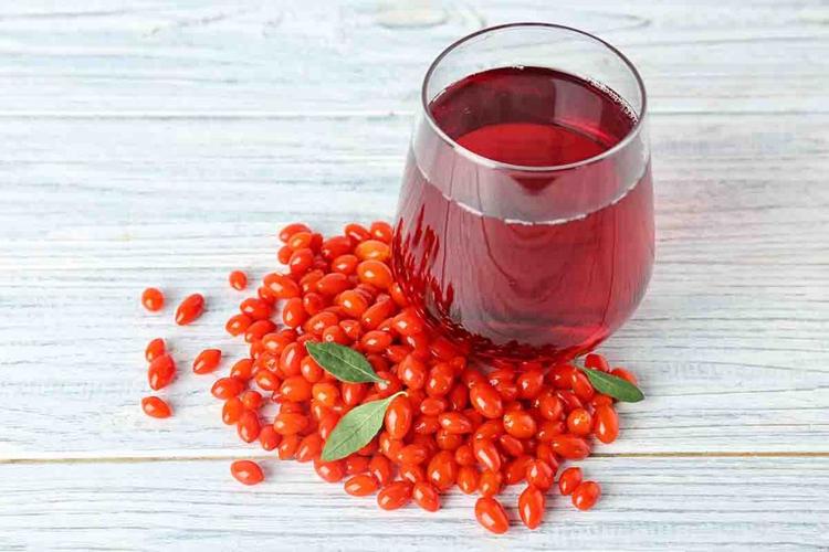 A glass of goji berry juice placed next to raw goji berries