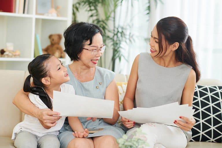 A middle-aged Asian woman sitting on a couch with her daughter and granddaughter, reading papers