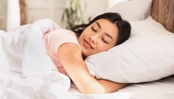 A woman sleeping comfortably under a comforter as she hugs her pillow tight