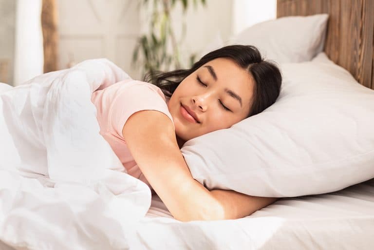 A woman sleeping comfortably under a comforter as she hugs her pillow tight