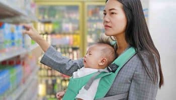 A mother carrying her baby in a front carrier while trying to choose groceries at a store