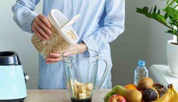 Woman pours oatmeal to a blender at a home kitchen environment