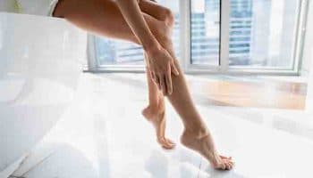 Woman sitting at the edge of a bathtub and caressing her lower leg