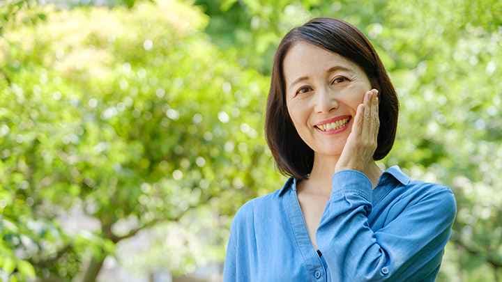 Middle-aged Asian woman touches her face while standing outside in nature