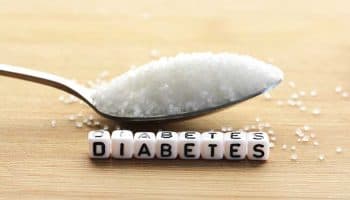 A spoon of sugar and block letters that spell ‘DIABETES’ on a wooden surface.