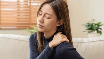 A woman holding her shoulder with one hand; a painful facial expression