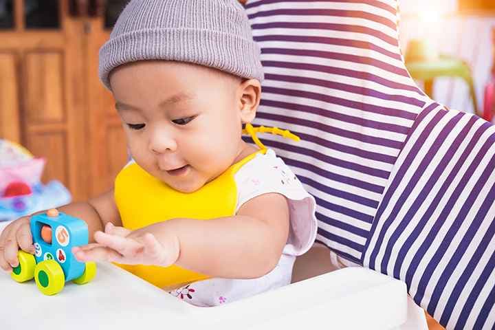 Toddler in a highchair playing with a wooden toy car