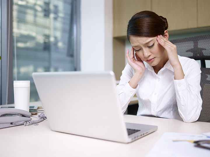 Woman in an office with her hands on her temples.