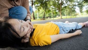 A woman supporting the head and neck of a girl lying unconscious on a pavement