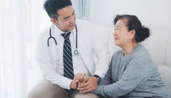 Woman holding a doctor’s hands as they both sit while he smiles at her