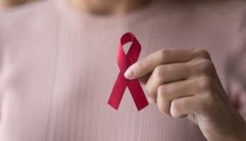 A close-up on a female hand holding a small red ribbon for HIV awareness.