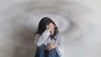 Woman sitting against a wall while supporting her forehead with her right hand