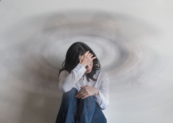 Woman sitting against a wall while supporting her forehead with her right hand