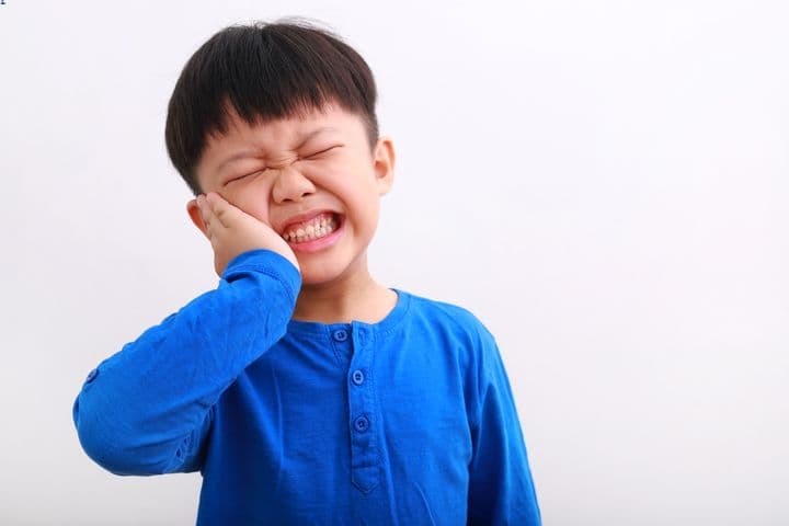 Little boy in blue shirt holds cheek due to toothache