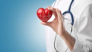 Man with a stethoscope around his shoulders holding a red-coloured, heart-shaped block with his left hand