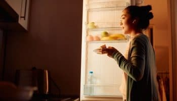 A woman standing in front of an opened refrigerator in a dark kitchen.