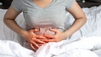 Woman holding her abdominal area with both hands while sitting up in bed