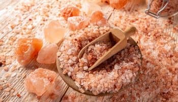 Himalayan salt in a bowl, big chunks of pink crystal on a wooden surface