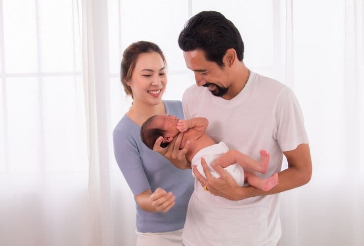 A father holding a baby with his wife standing next to him.