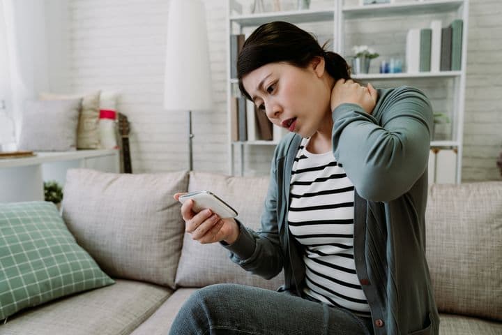 Poor sitting posture is causing stiff neck pain to woman