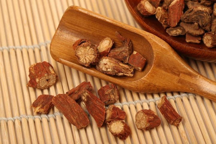 Cut red sage roots displayed on a bamboo mat, and a wooden plate and spoon