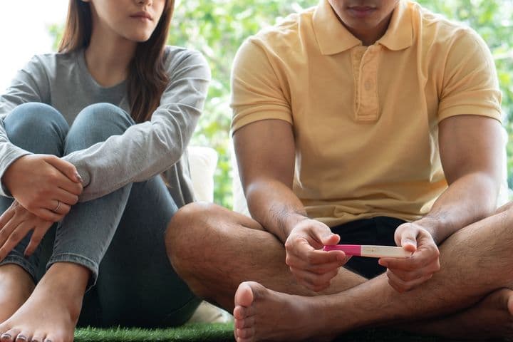 A partial view of a couple with the man holding a pregnancy test