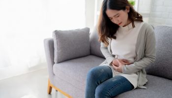 Women holds stomach in pain while sitting on couch.