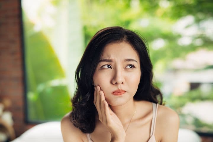 Woman holding the right side of her jaw as she looks to the left 