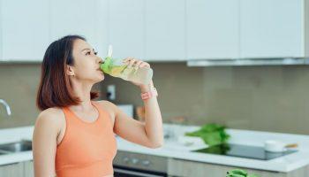 A woman drinking a bottle of lemon and cucumber infused water