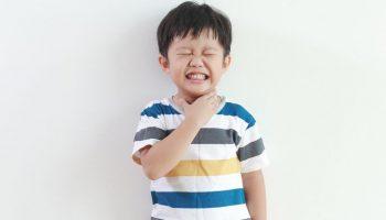 Asian boy with sore throat touching his neck.