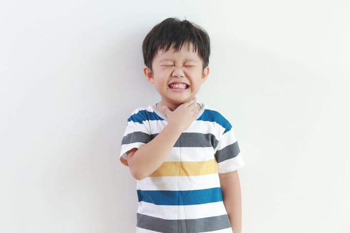 Asian boy with sore throat touching his neck.