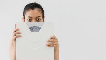 A woman covering half of her face with a weight scale.