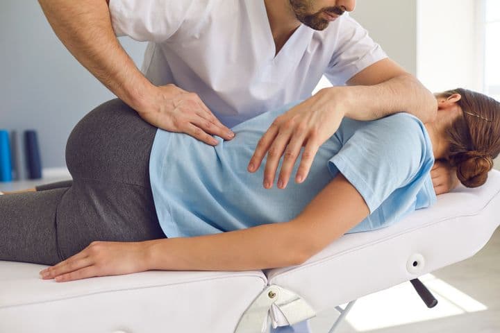 A chiropractor treats a woman’s back as she lies on a procedure chair