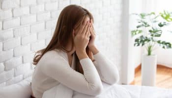 Woman holding her face in her hands while sitting up in bed