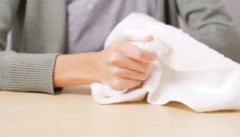 Woman holding a white towel with her right hand as she sits at a table