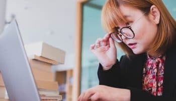 Woman lowering her glasses with her right hand to look at her laptop