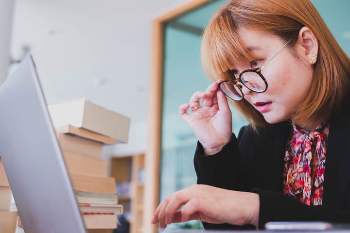 Woman lowering her glasses with her right hand to look at her laptop