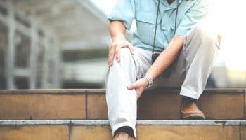 Man holding his right knee with both hands as he sits on the top step of a staircase