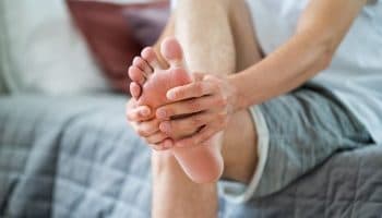 A partial view of a man holding the back of his foot in pain.