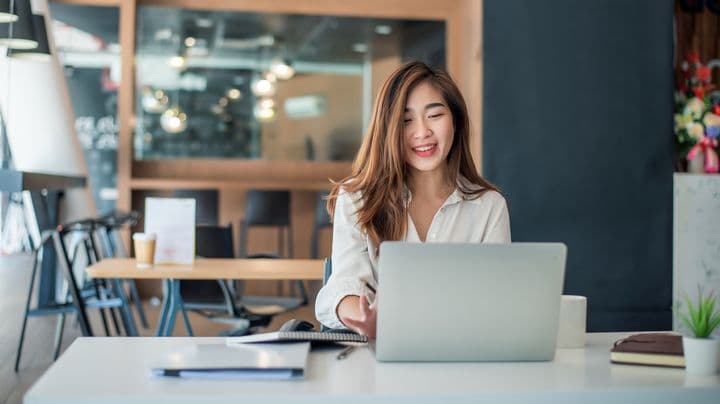 Woman smiling while sitting at a table and using a laptop