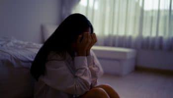 Woman sitting next to her bed with her face in her hands