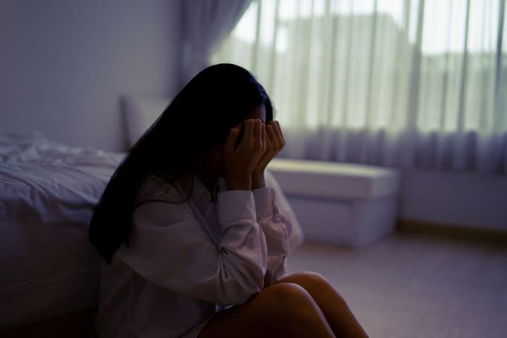 Woman sitting next to her bed with her face in her hands