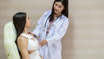 Healthcare provider examining a woman’s breasts as she sits up in a white chair