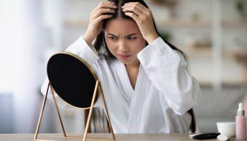 A young woman looking stressed while checking her scalp for white hair.