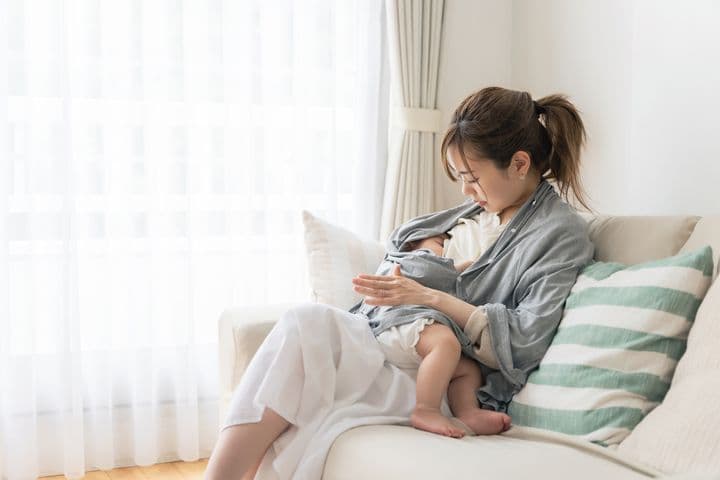 Woman sitting on a sofa while breastfeeding her child.