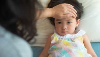 A mother checks a feverish toddler’s forehead.