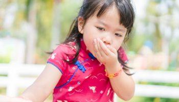 Little girl puts one hand over her mouth with a vomiting motion.